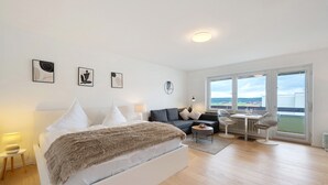 A modern bedroom with a bed, a sofa, a small table, and artwork on the wall.