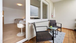 A balcony with a table and chairs, a window, and a view of the sky.