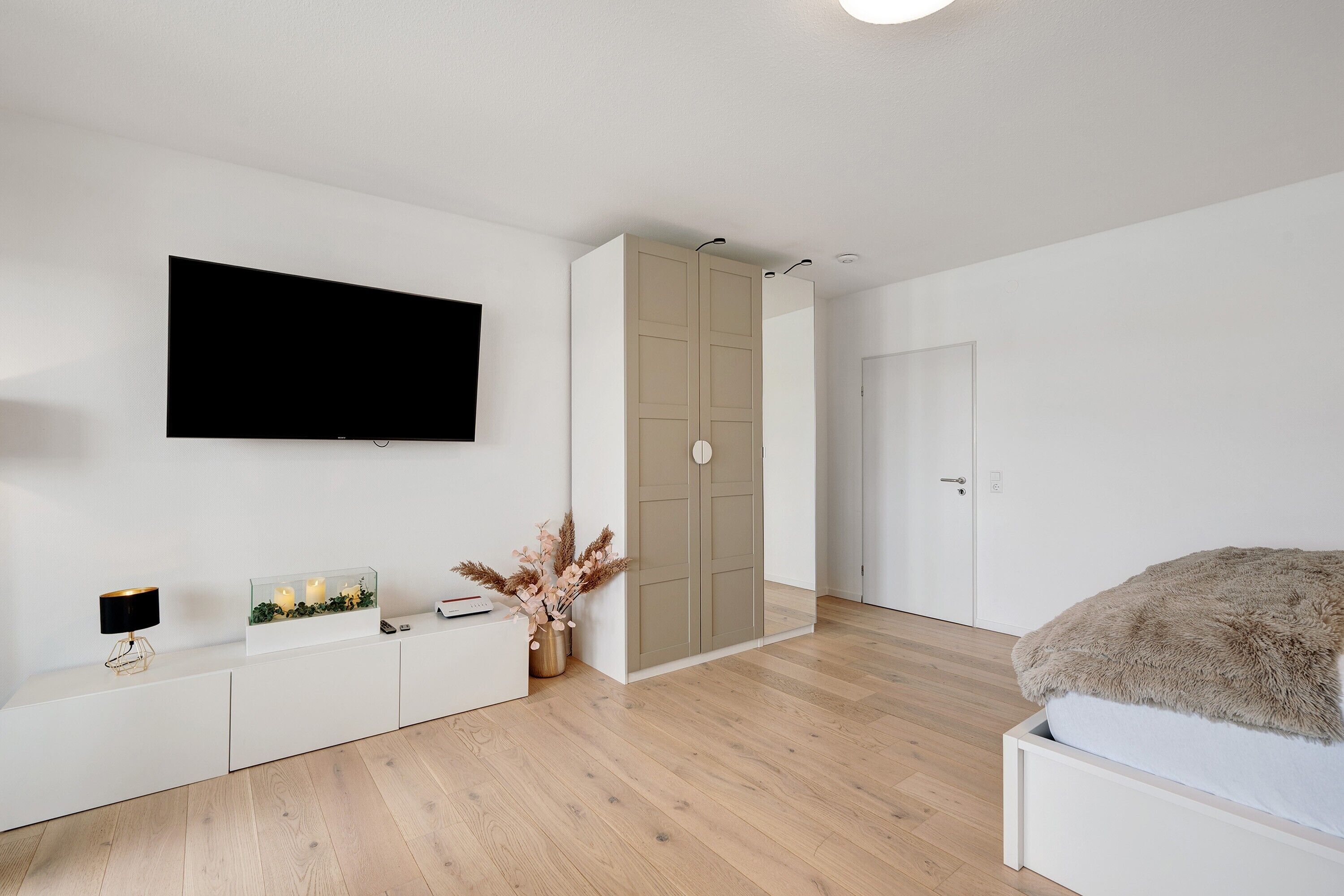 Une chambre à coucher moderne, comprenant un lit, une télévision, une armoire et une table de chevet avec une lampe et des objets décoratifs.