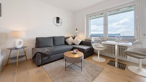 A modern living room with a grey sofa, a round coffee table, a lamp, and a view of the sea through large windows.