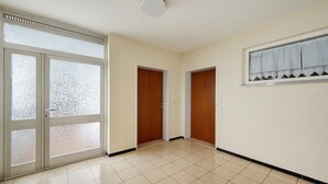 A hallway with a tiled floor, a glass door with frosted glass panels, and two wooden doors.