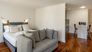 Ein modernes Wohnzimmer mit grauem Sofa, einem Essbereich mit weißem Tisch und Stühlen sowie einer Küche im Hintergrund.