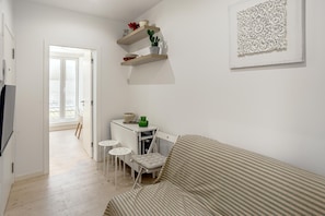 A small, bright room with a bed, a desk, and two chairs. There are shelves with decorative items and a framed artwork on the wall. - Downtown Modern Apartments by Homing (Lisbon)