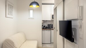 A compact living space with a sofa, a flat-screen TV mounted on the wall, a kitchen area with modern appliances, and a pendant light. - Downtown Modern Apartments I by Homing (Lisbon)