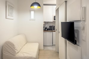 A compact living space with a sofa, a flat-screen TV mounted on the wall, a kitchen area with a dishwasher, and a pendant light. - Downtown Modern Apartments I by Homing (Lisbon)