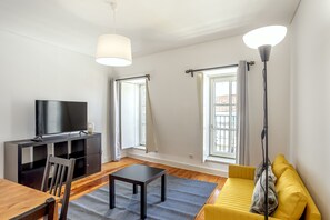 A living room with a TV, sofa, table, and floor lamp. - Bairro Alto Typical by Homing (Lisbon)