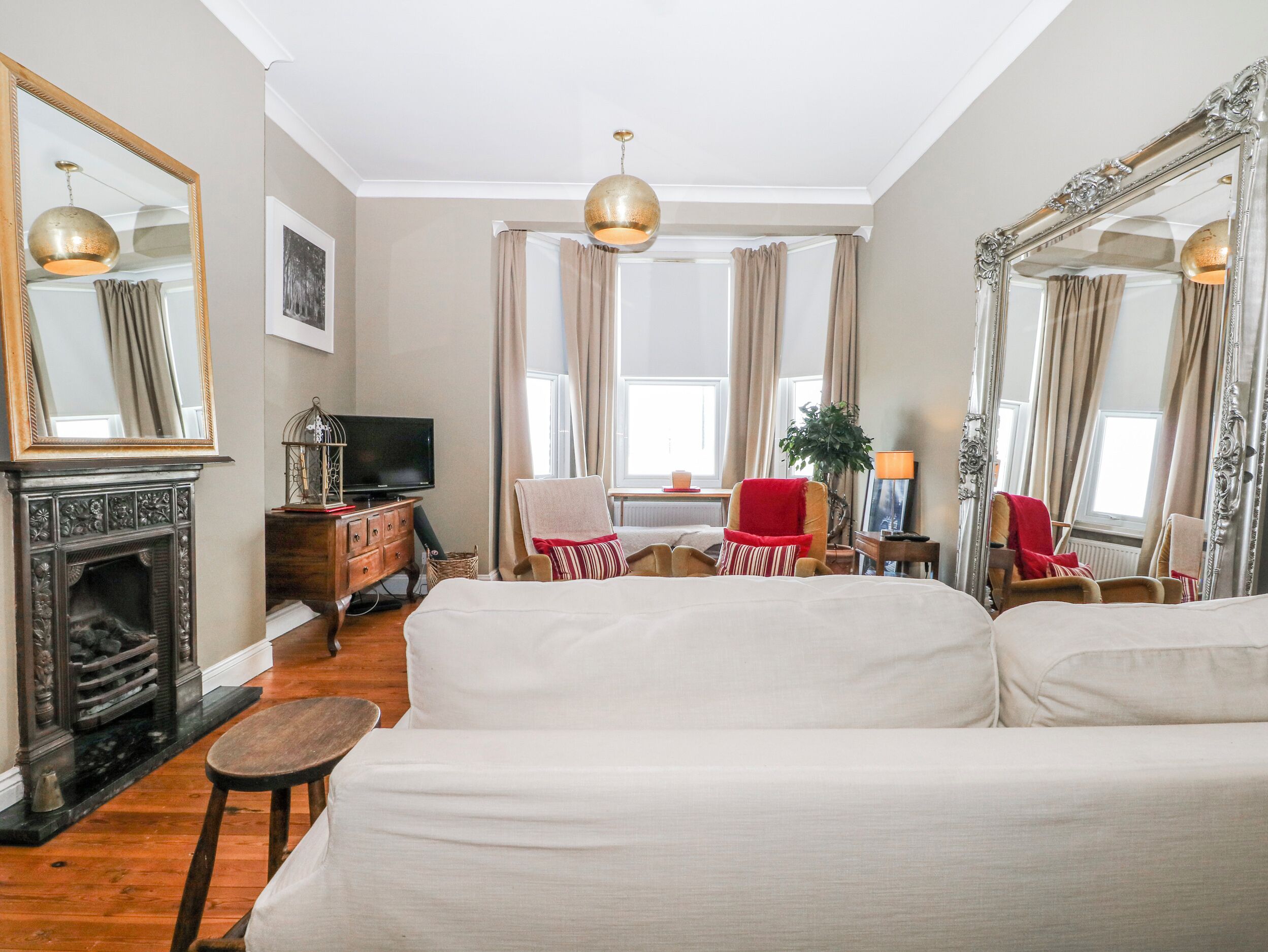 A living room with a fireplace, sofa, chairs, a television, and large mirrors.