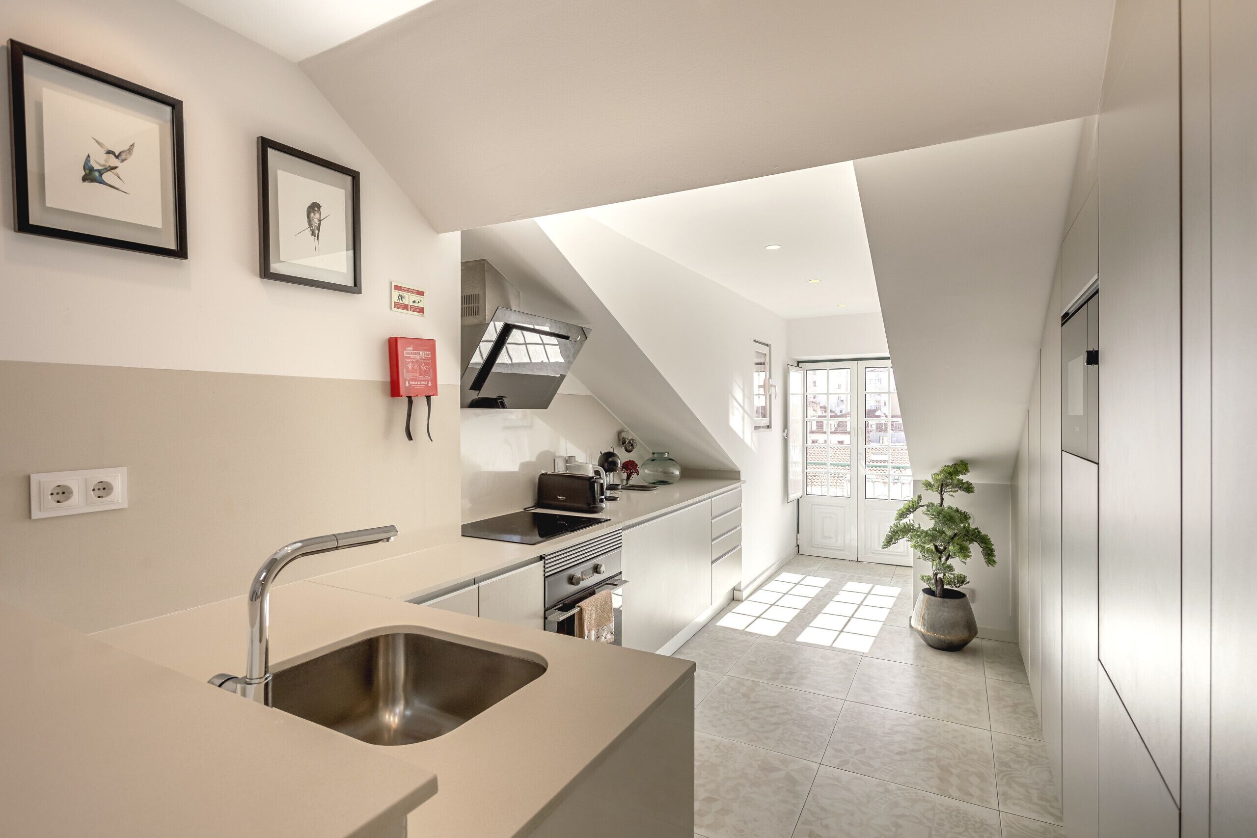 Une cuisine moderne dotée d’un grand îlot central, d’un évier en acier inoxydable et d’un four encastré. Un escalier mène à un balcon offrant une vue sur la ville.