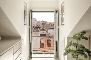 Una escalera estrecha que lleva a un balcón con barandilla de metal, una pequeña planta en maceta y vistas de edificios de colores.