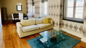 A living room with a sofa, a glass coffee table, a dining area with a table and chairs, and patterned wallpaper. - Downtown Riverside III by Homing (Lisbon)