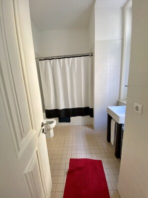 A bathroom with a toilet, a shower curtain, a sink, and a red rug. - Downtown Riverside III by Homing (Lisbon)