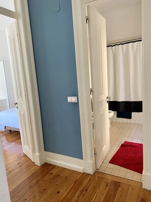 A room with a blue wall, wooden flooring, a white door, a white toilet, and a red rug. - Downtown Riverside III by Homing (Lisbon)