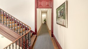 A hallway with a wooden staircase, a red door, and a framed painting on the wall. - Downtown Riverside III by Homing (Lisbon)
