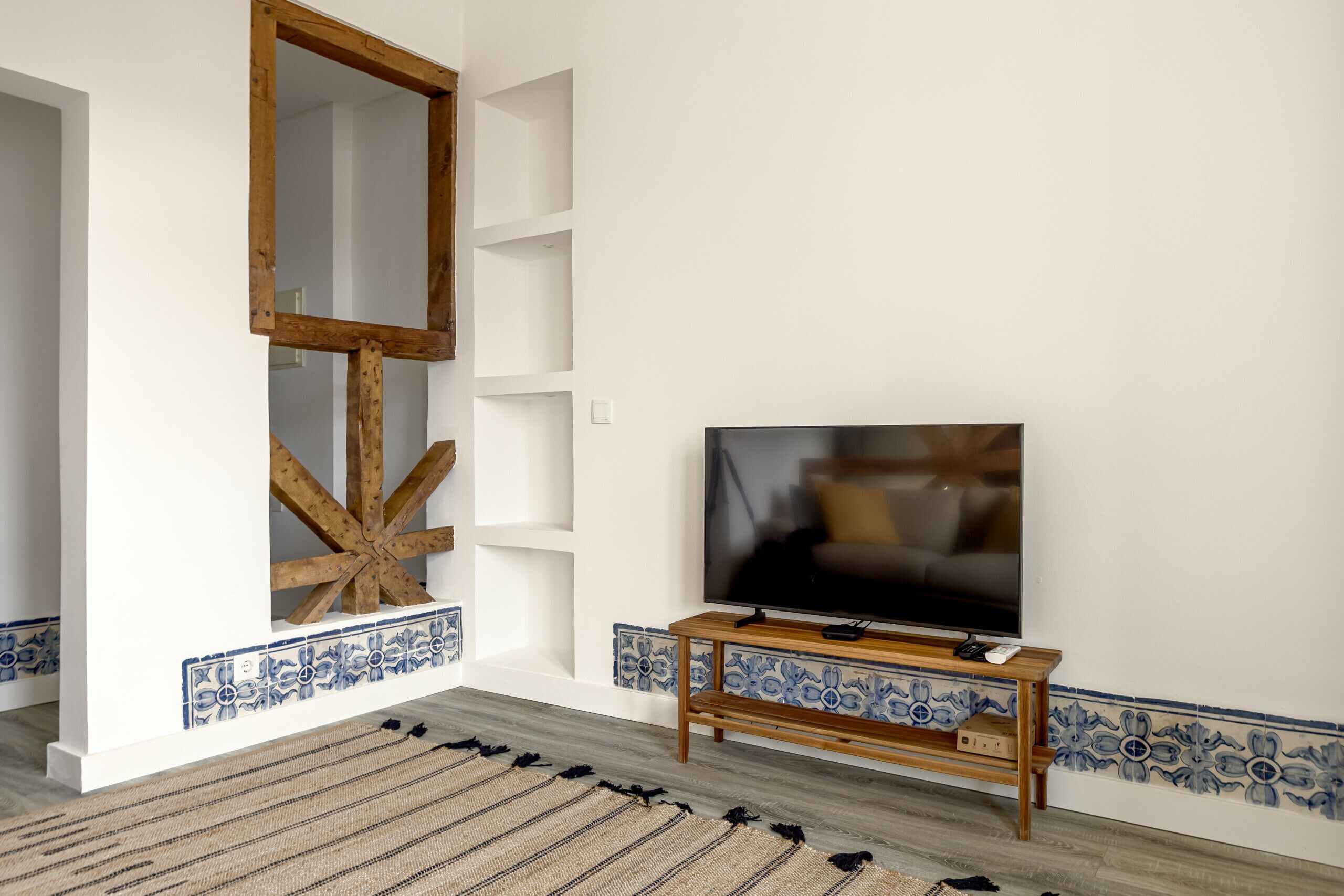 A room with a television on a wooden stand, a large wooden-framed mirror, and patterned tile borders.