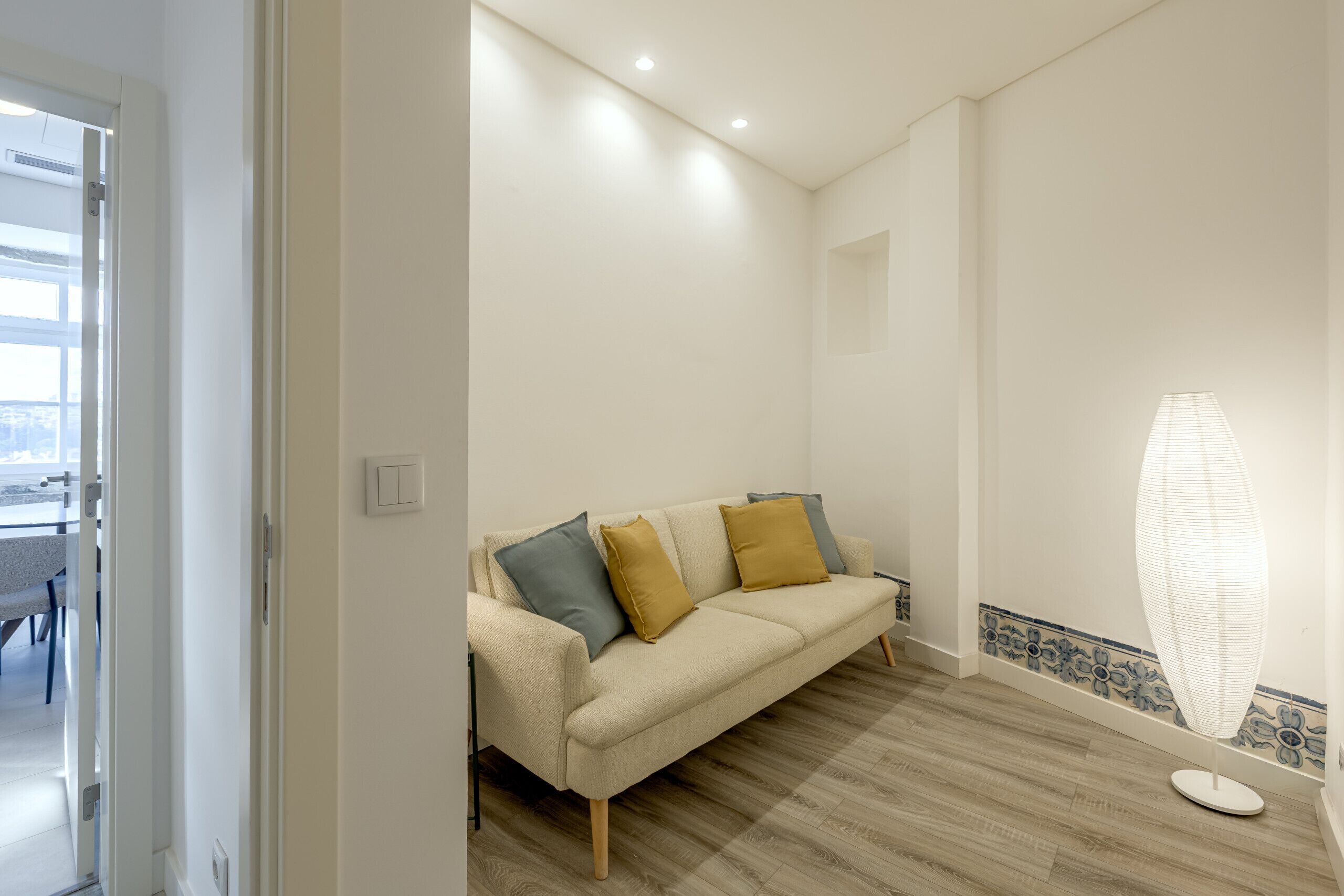 Un salón en tonos neutros con un sofá, una lámpara de pie y un borde decorativo en la pared.