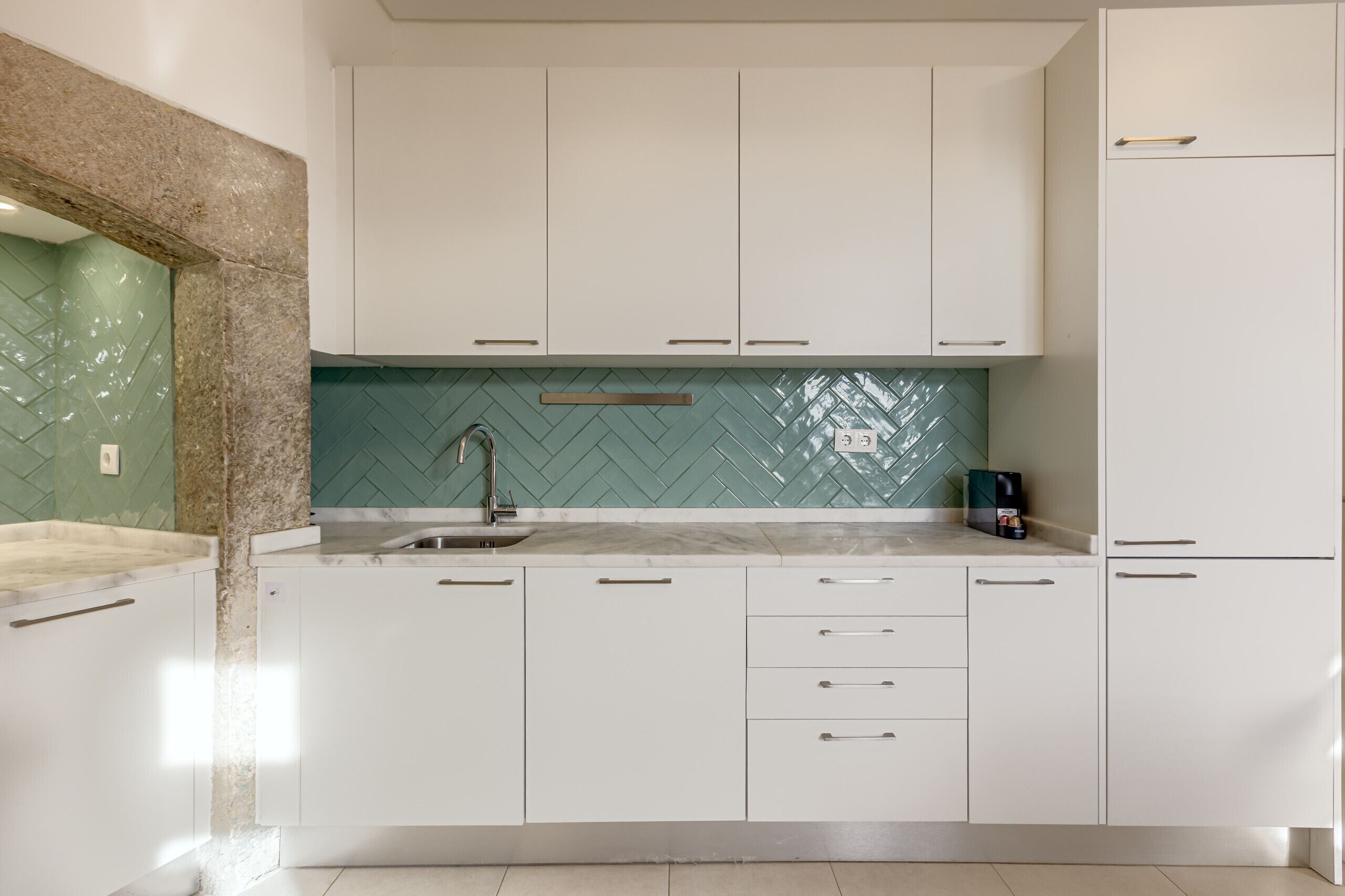 Una cocina moderna con armarios blancos, salpicadero de mosaicos tipo espiga y un lavamanos de acero inoxidable.