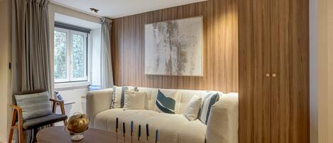 A modern living room with a wooden panel wall, a beige sofa with blue accents, a wooden coffee table, and a large abstract painting.