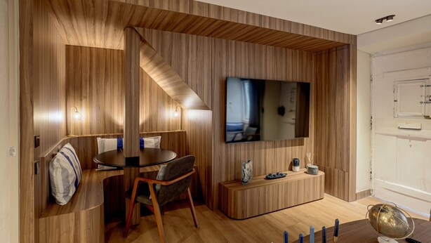 A modern living room with a wooden accent wall, a flat-screen TV, a dining area, and a small seating space. - Principe Real Prime by Homing (Lisbon)
