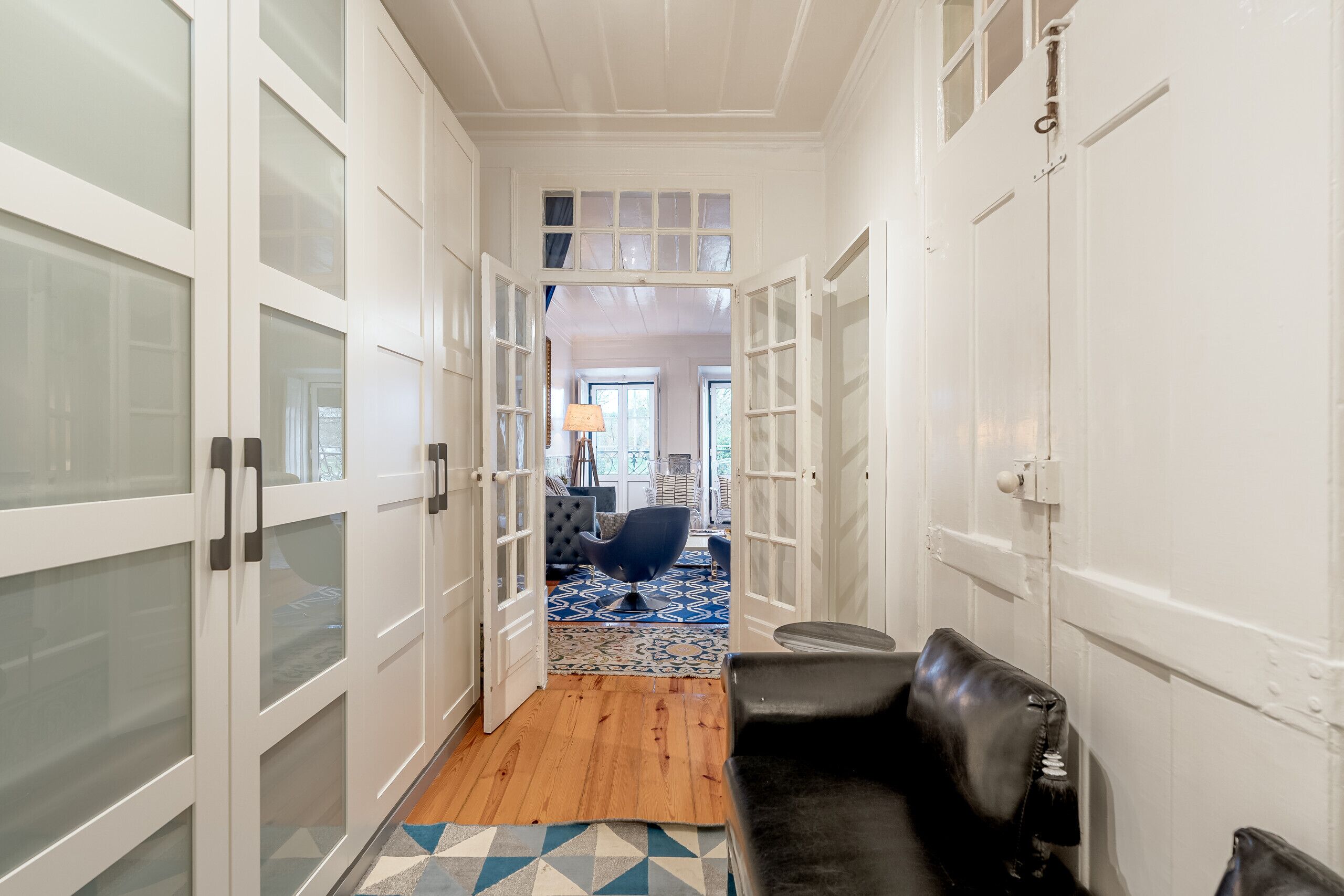 A hallway with white doors, a black leather sofa, and a patterned rug.