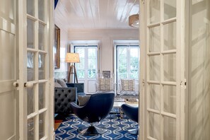 A room with a patterned floor, a dark upholstered chair, a lamp, and a view through a door. - Belem Historical by Homing (Lisbon)