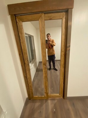 Ein Zimmer mit einem spiegelnden, holzgerahmten Spiegel, einer Tür und einem Fenster.