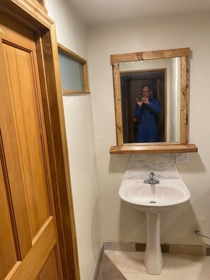 Een badkamer met een houten deur, een witte wastafel en een spiegel met houten omlijsting.