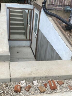 Eine Betonkonstruktion mit einer Metalltreppe, die zu einer Tür führt, umgeben von Kies und Ziegelsteinen.