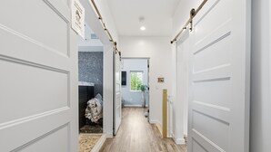 Un couloir avec des portes blanches, un plancher en bois et une vue sur une pièce dont le mur est décoré d’un motif.