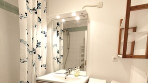 Een badkamer met douche, wastafel, spiegel en een wasmachine.