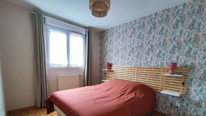 Een slaapkamer met een bed, een raam met gordijnen, een radiator en bloemenbehang.