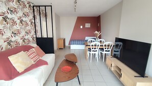 Een woonkamer met een bank, een salontafel, een televisie, een eethoek met stoelen, een bed en een wand met een bloemenmotief.