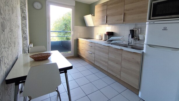 Een keuken met een eettafel, stoelen, een koelkast en een raam met uitzicht op groen.