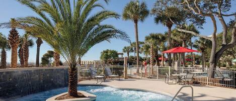 A pool area with palm trees, lounge chairs, and a red umbrella.