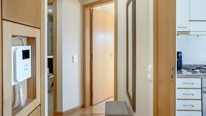 Un pasillo con armarios de madera, un banco, una puerta que da a un baño y una zona de cocina con estufa.