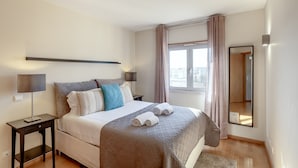 Un dormitorio con cama, mesitas de noche, un espejo y una ventana con cortinas.