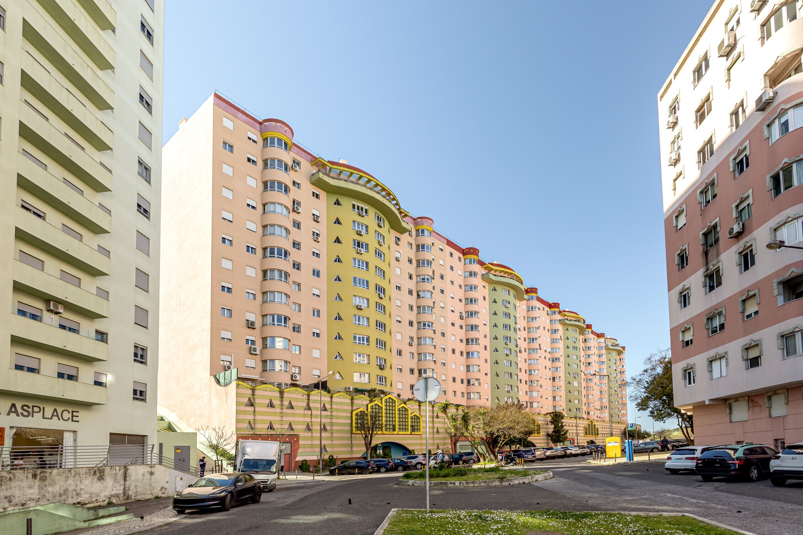 Un edificio residencial de varios pisos con balcones, entrada protegida por un portón y zona de estacionamiento.