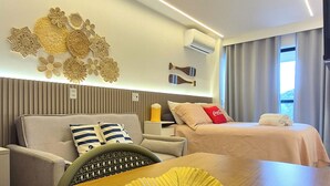 Een moderne hotelkamer met een bank, een bed, een eettafel met een decoratieve schaal, en een wand met een lamp en decoratie.