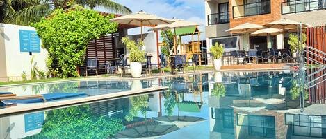 Zona de piscina con vista despejada, sillas de descanso y un edificio de varios pisos con balcones.