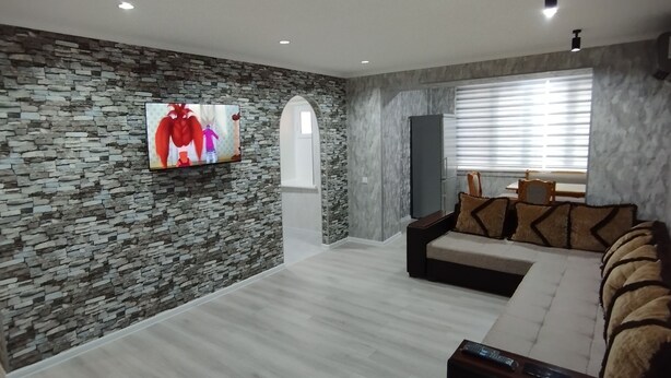 Ein modernes Wohnzimmer mit Steinwand, Flachbildfernseher, einer Couch und einem Fenster mit Jalousien.