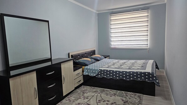 Une chambre à coucher avec un lit, une commode, un miroir et une fenêtre avec des stores.
