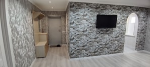 Un couloir avec un mur en pierre, un téléviseur fixé au mur et un meuble en bois.