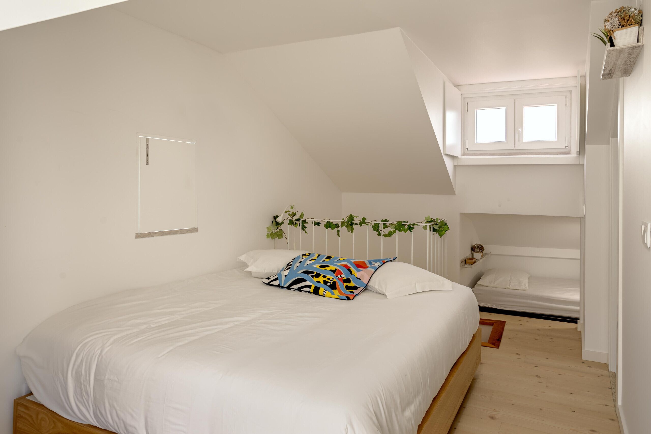 A bedroom with a large bed, a window, a plant, and a bunk bed in the corner.
