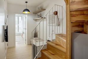 Un escalier avec des marches en bois et des rampes en métal, un luminaire suspendu et une étagère fixée au mur, ornée d’objets décoratifs.