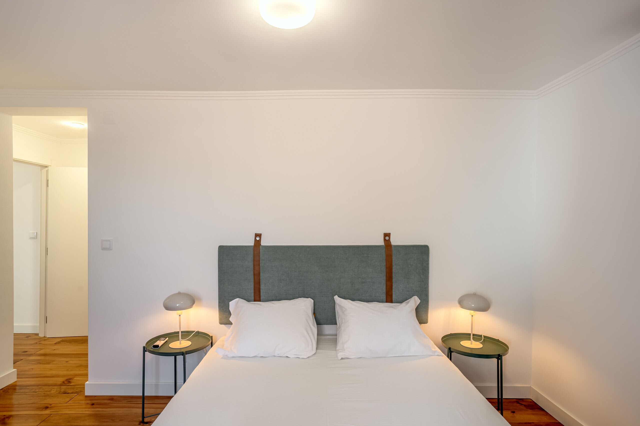 Un dormitorio con una cama, dos mesitas de noche con lámparas y un cabecero.