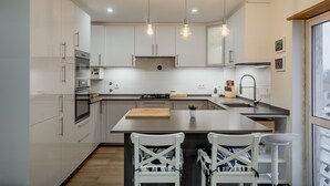 A modern kitchen with white cabinets, a central island, and pendant lighting. - Carcavelos Modern Apartment by Homing (Cascais)