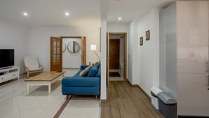 A modern living room with a blue sofa, wooden coffee table, and a TV. There is a white cabinet and a trash bin. - Carcavelos Modern Apartment by Homing (Cascais)
