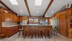 Una cocina con armarios de madera, una isla central con taburetes y un tragaluz.