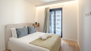 A bedroom with a bed, pillows, a blanket, a bedside table, a window, and a view of buildings outside. - Modern Lisbon W/ Balcony Pool II (Lisbon)