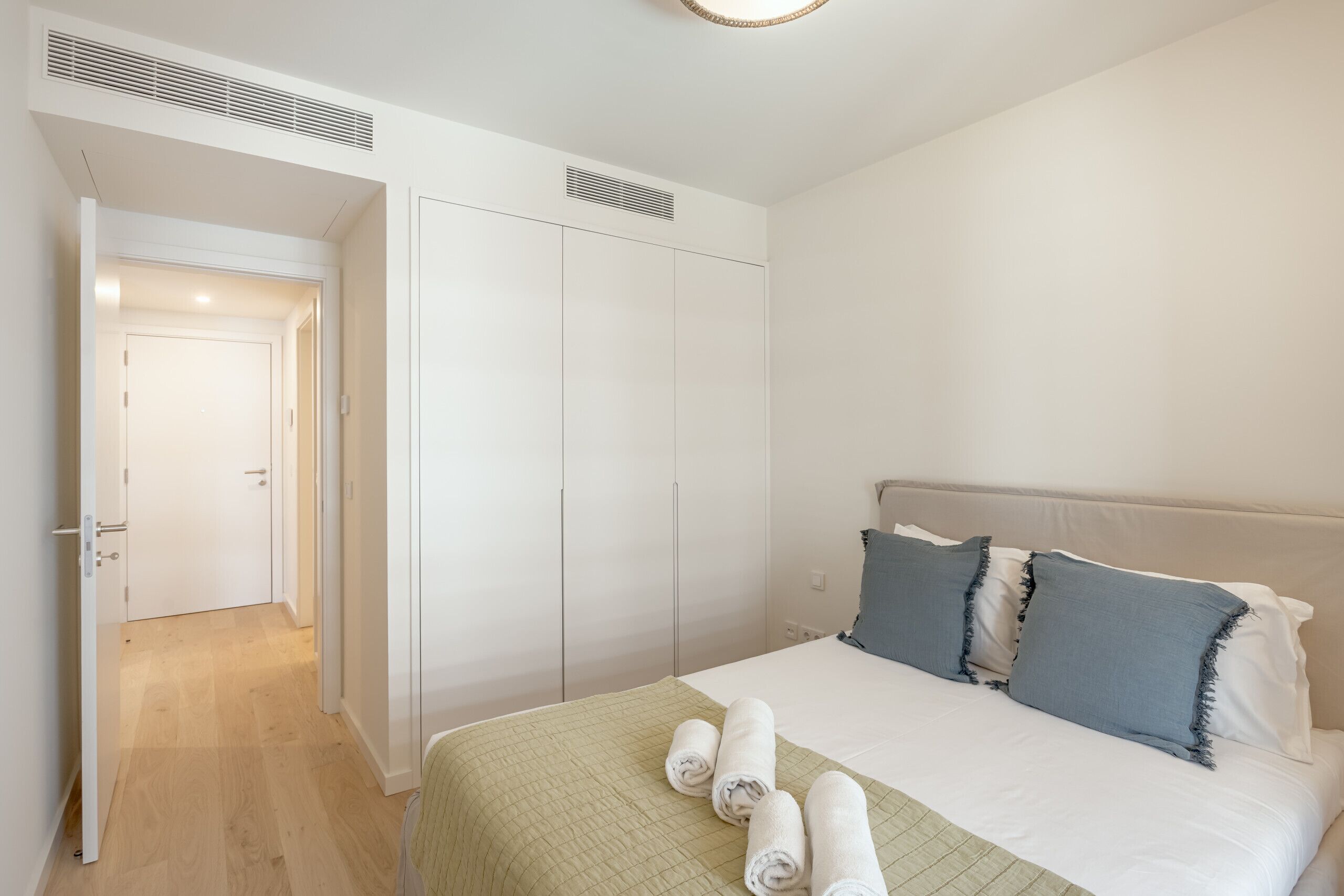 Een slaapkamer met een bed, kussens, een groene deken en een deur naar een andere kamer.