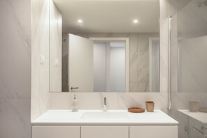 A modern bathroom with a white vanity, a mirror, a shower enclosure, and a marble wall. - Modern Lisbon W/ Balcony Pool II (Lisbon)